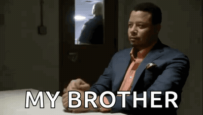 A Man In A Suit And Tie Is Sitting At A Table With The Words My Brother Written On It . GIF