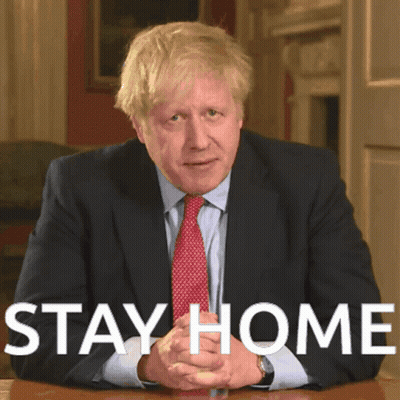A Man In A Suit And Tie Is Sitting At A Table With The Words " Stay Home " Written Above Him GIF