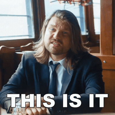 A Man In A Suit And Tie Is Sitting At A Table With The Words " This Is It " Written Below Him GIF