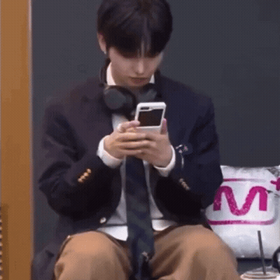 A Man In A Suit And Tie Is Sitting Down Looking At His Phone . GIF