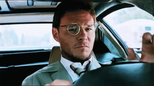 A Man In A Suit And Tie Is Sitting In A Car Looking Out The Window . GIF