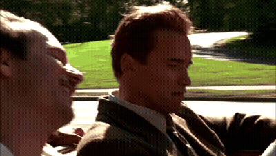 A Man In A Suit And Tie Is Sitting In A Car With Another Man GIF