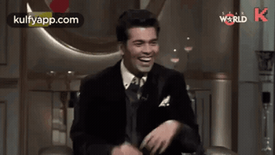A Man In A Suit And Tie Is Sitting In A Chair And Laughing . GIF