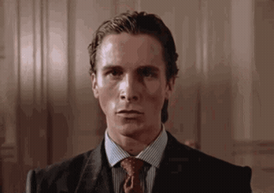 A Man In A Suit And Tie Is Sitting In A Chair And Looking At The Camera . GIF