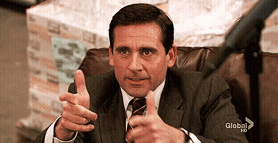 A Man In A Suit And Tie Is Sitting In A Chair And Pointing At The Camera . GIF