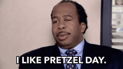 A Man In A Suit And Tie Is Sitting In A Chair And Saying `` I Like Pretzel Day . '' GIF