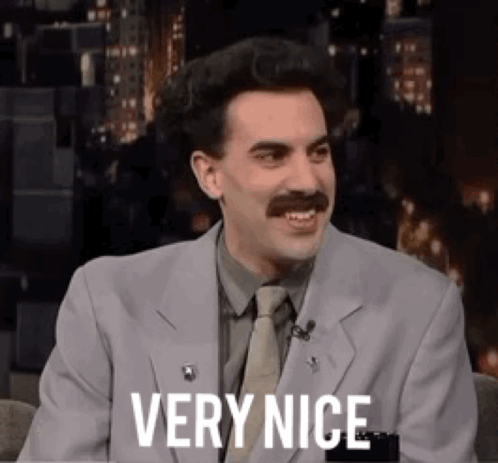 A Man In A Suit And Tie Is Sitting In A Chair And Smiling . GIF