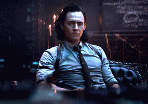 A Man In A Suit And Tie Is Sitting In A Chair In A Dark Room GIF
