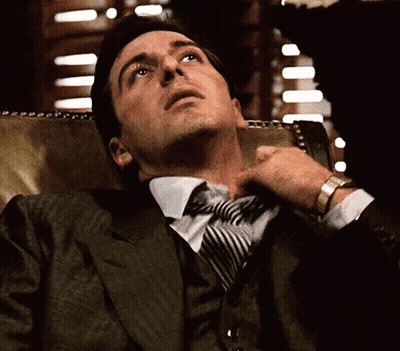 A Man In A Suit And Tie Is Sitting In A Chair GIF