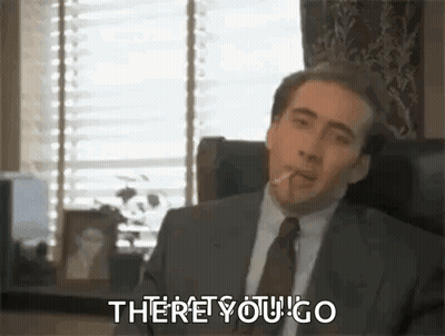 A Man In A Suit And Tie Is Sitting In A Chair Smoking A Cigarette And Saying `` There You Go '' . GIF
