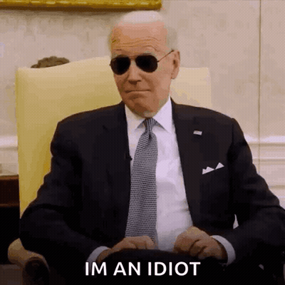 A Man In A Suit And Tie Is Sitting In A Chair Wearing Sunglasses And Making A Funny Face . GIF