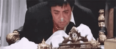 A Man In A Suit And Tie Is Sitting In A Chair With A Napkin In His Nose . GIF