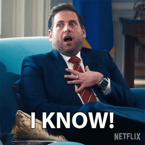 A Man In A Suit And Tie Is Sitting In A Chair With His Hand On His Chest And Says " I Know " GIF