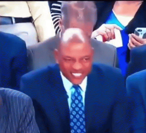A Man In A Suit And Tie Is Sitting In A Crowd GIF