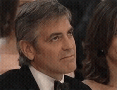 A Man In A Suit And Tie Is Sitting In A Crowd Of People And Looking To The Side . GIF