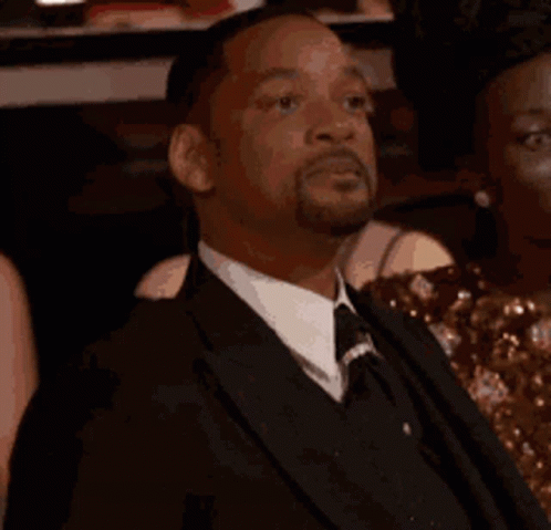 A Man In A Suit And Tie Is Sitting In A Crowd Of People And Saying Yes . GIF