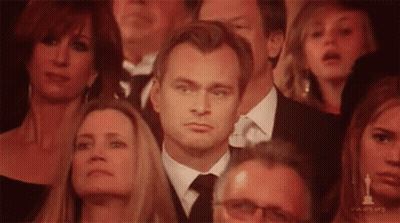 A Man In A Suit And Tie Is Sitting In A Crowd Of People Watching A Movie . GIF
