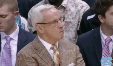 A Man In A Suit And Tie Is Sitting In A Crowd With A Nc Logo In The Background GIF
