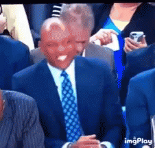 A Man In A Suit And Tie Is Sitting In A Crowd With His Tongue Out GIF