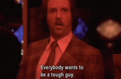 A Man In A Suit And Tie Is Sitting In A Dark Room And Says Everybody Wants To Be A Tough Guy . GIF
