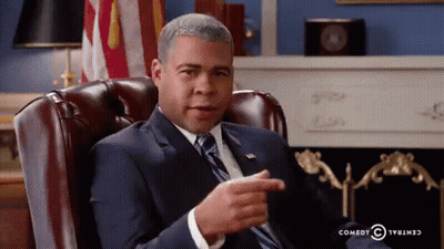 A Man In A Suit And Tie Is Sitting In A Leather Chair And Pointing GIF