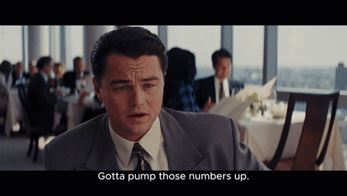 A Man In A Suit And Tie Is Sitting In A Restaurant And Says Gotta Pump Those Numbers Up GIF