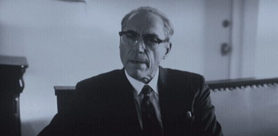 A Man In A Suit And Tie Is Sitting In A Room GIF