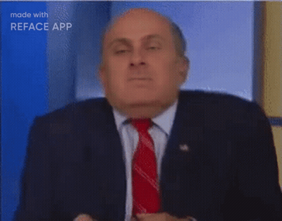 A Man In A Suit And Tie Is Sitting In Front Of A Blue Background . GIF