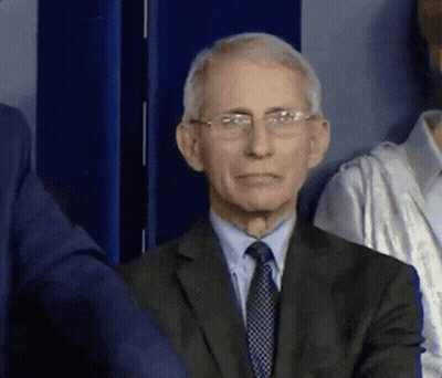 A Man In A Suit And Tie Is Sitting In Front Of A Blue Wall . GIF