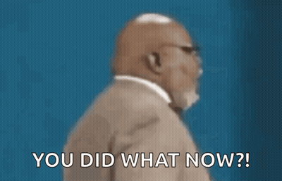 A Man In A Suit And Tie Is Sitting In Front Of A Blue Wall . GIF