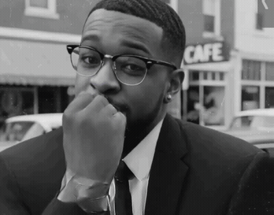A Man In A Suit And Tie Is Sitting In Front Of A Cafe Sign GIF