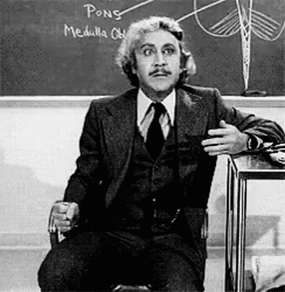 A Man In A Suit And Tie Is Sitting In Front Of A Chalkboard That Says Pong Medulla GIF