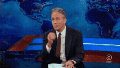 A Man In A Suit And Tie Is Sitting In Front Of A Comedy Central Sign GIF