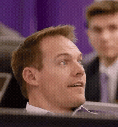 A Man In A Suit And Tie Is Sitting In Front Of A Computer Screen Looking Up . GIF