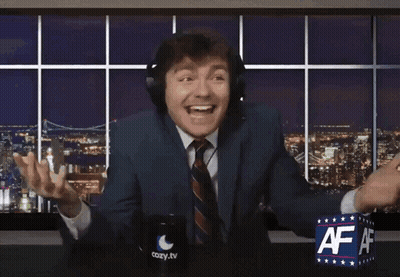A Man In A Suit And Tie Is Sitting In Front Of A Cozy Tv Sign GIF