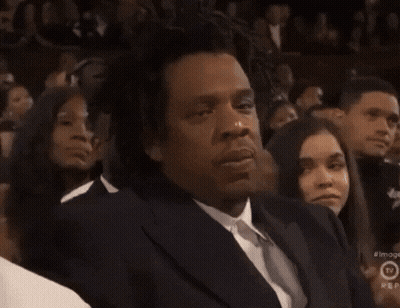 A Man In A Suit And Tie Is Sitting In Front Of A Crowd And A Sign That Says Rep On It GIF