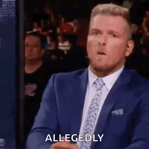 A Man In A Suit And Tie Is Sitting In Front Of A Crowd . GIF