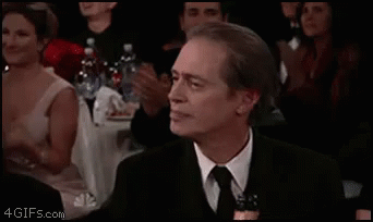 A Man In A Suit And Tie Is Sitting In Front Of A Crowd Of People Clapping . GIF