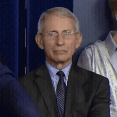A Man In A Suit And Tie Is Sitting In Front Of A Crowd . GIF