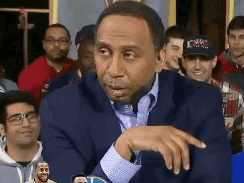 A Man In A Suit And Tie Is Sitting In Front Of A Group Of People . GIF