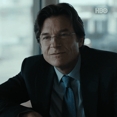 A Man In A Suit And Tie Is Sitting In Front Of A Hbo Logo GIF