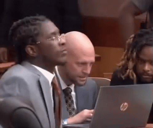 A Man In A Suit And Tie Is Sitting In Front Of A Laptop . GIF