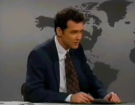 A Man In A Suit And Tie Is Sitting In Front Of A Map Of The World . GIF