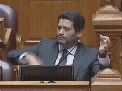 A Man In A Suit And Tie Is Sitting In Front Of A Microphone GIF
