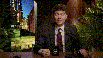 A Man In A Suit And Tie Is Sitting In Front Of A Microphone With A Mug That Says Af GIF