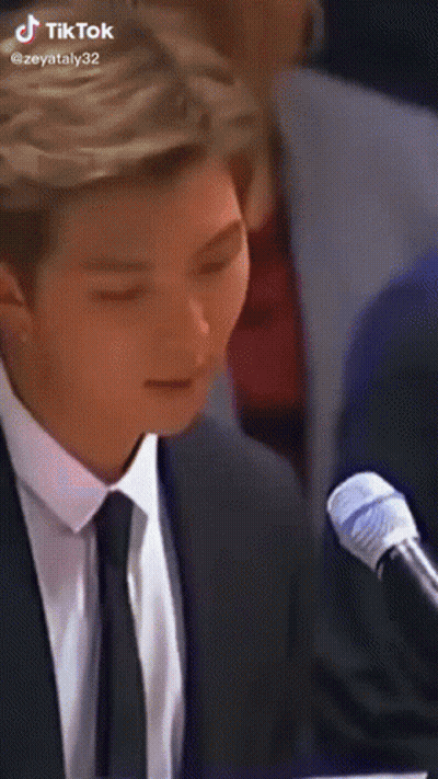 A Man In A Suit And Tie Is Sitting In Front Of A Microphone With His Eyes Closed . GIF