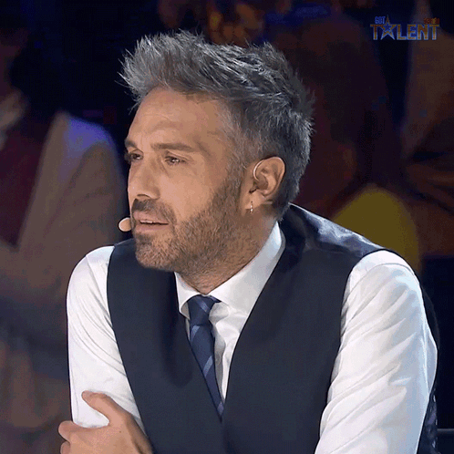 A Man In A Suit And Tie Is Sitting In Front Of A Microphone With The Word Talent Above Him GIF
