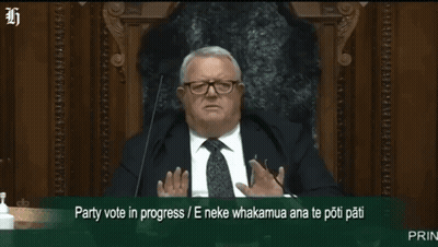 A Man In A Suit And Tie Is Sitting In Front Of A Microphone With The Words Party Vote In Progress Written Below Him GIF