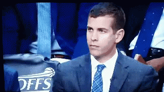A Man In A Suit And Tie Is Sitting In Front Of A Offs Sign GIF