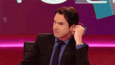 A Man In A Suit And Tie Is Sitting In Front Of A Purple Screen . GIF